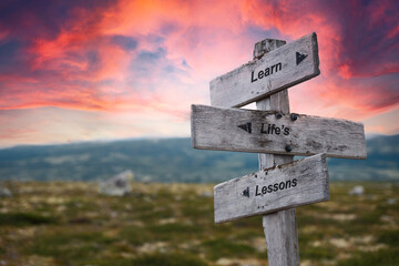 learn lifes lessons text quote on wooden signpost outdoors in nature. Pink dramatic skies in the background.
