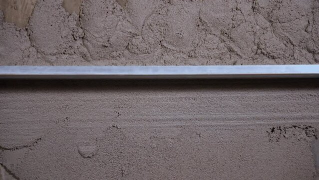 A man with an even long spatula cement dry mixture on the wall. Close-up. Align the cement mixture with a special tool