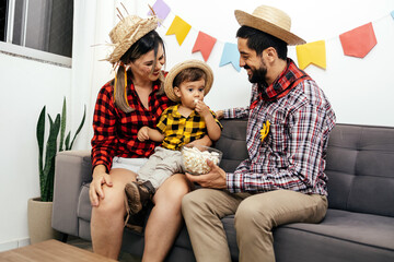 Brazilian Junina party at home. Family celebrating Festa Junina in the living room, wearing typical clothes and the wall decorated with colorful flags.