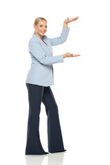 Middle aged advertising senior business woman in blue jacket and black trousers posing on white...
