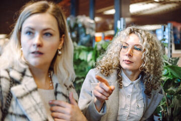 Two girlfriends, work colleagues are interested in considering assortment of garden center and decide what to watch. 