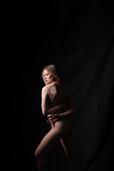 Ballerina in a beige bodysuit. Dark background. Sculpted beautiful female body. Pose of a gymnast.