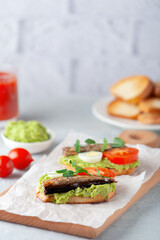 Sandwiches with sprats on toasted slices of bread. Sandwich with smoked sprat - fish, avocado and tomato.
