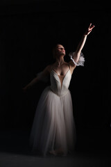 Naklejka premium Professional ballerina dancing ballet.Ballerina in a white dress and pointe shoes. Dark background. Beautiful female body.