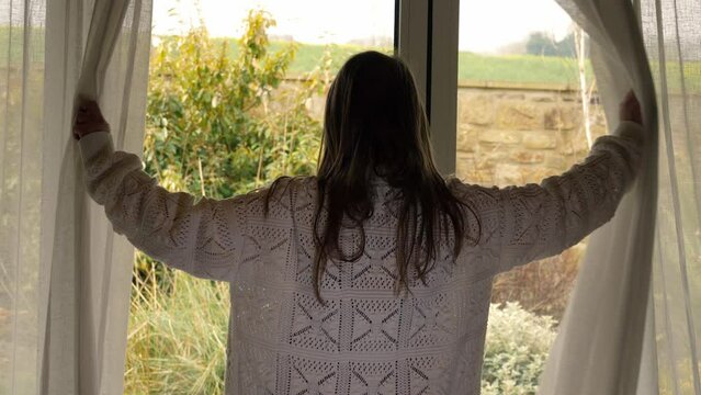 Woman opening curtains in room to summer day 