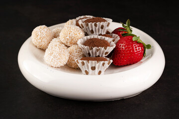 On a dark background, different candies and strawberries on a light plate.