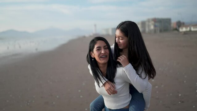 mother and daughter having fun piggyback spinning laughing on the beach