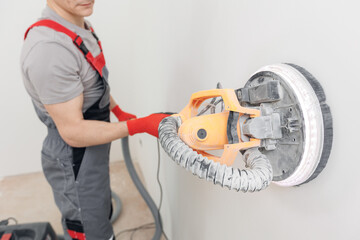 Painter work with white wall polishing and sanding surface after putty for painting. Automation...