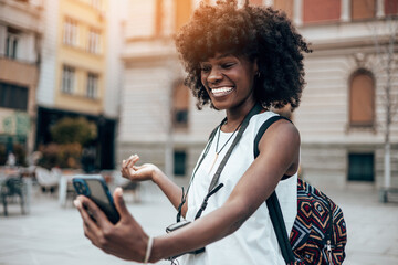 Young black female tourist enjoys walking through the streets of a beautiful European city. She is happy and using her smart phone to take some photos and videos. Bright sunny day.