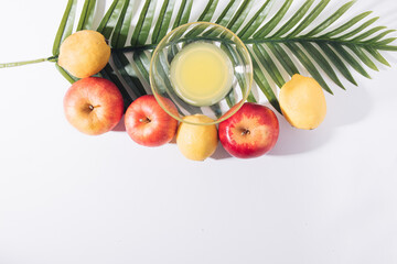 Summer tropical layout made of fresh organic fruit, a green tropical palm leaf, and a glass of cocktail on a white background with copy space. Minimal nature flat lay.