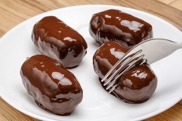 Chocolate dessert in a shiny glaze on a white plate standing on a wooden table. 