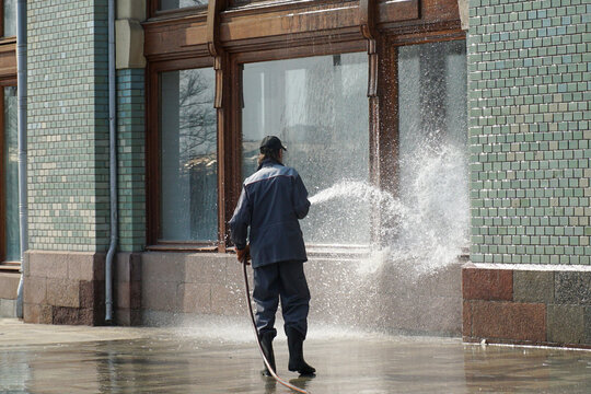 A uniformed worker washes a house window with a powerful jet of water.