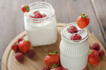 Strawberry raspberry yogurt in jar on wooden board close-up and copy space