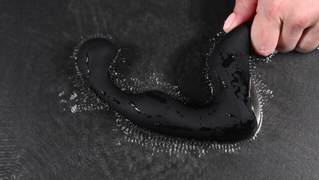A woman holds a black prostate stimulator that vibrates and creates ripples on the surface of the water against a black background.