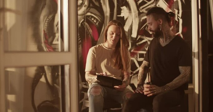 Female tattooist showing tattoo pictures to male client