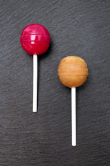 Fototapeta na wymiar Two red and caramel colored lollipops lie on a rough black background. Classic sweet candies on a stick. Sweet dessert concept for kids