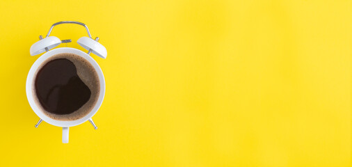 Black coffee on the dial of the white alarm clock on the yellow background. Copy space. Top view.