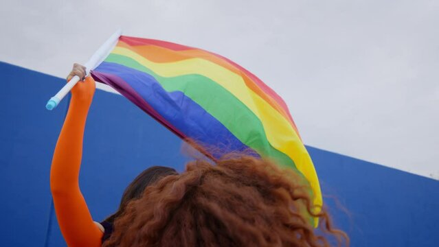 Young cheerful Latin drag queen waving rainbow flag on gay pride parade day. Transgender people celebrating LGBT free love festival. 
