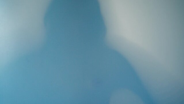 Shadow Blur of a horror man behind frosted glass. Blurred hand, body shape abstraction and one palm. Reflection of the silhouette through the light.