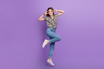 Full body portrait of excited cheerful lady jumping arms fingers show v-sign isolated on purple color background