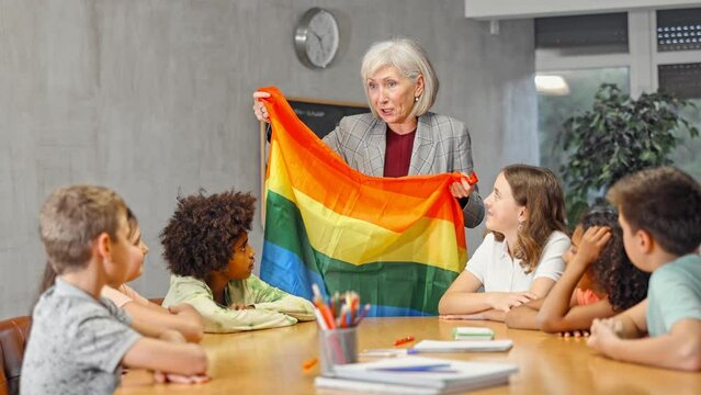 Kids learning together about lgbt pride in social sicences class Female teacher showing rainbow flag to kids in geography . High quality 4k footage
