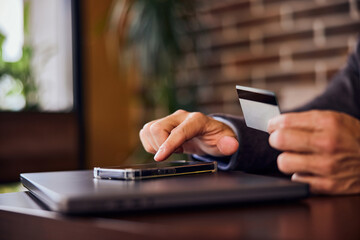 Close-up of a male paying online, holding a card, using his mobile phone.
