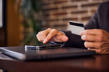 Male hands touching a phone while holding a card with other hand.