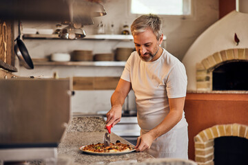 Photo of a pizza maker, dressed in a white uniform, making a pizza for his customers.