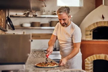  Photo of a pizza maker, dressed in a white uniform, making a pizza for his customers. © bnenin