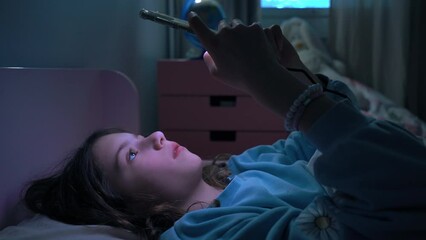 Teen girl scrolling social media texting on smartphone in bed in bedroom at night. Technology, internet, communication and people concept. Dependence on social networks in children. Not healthy sleep.