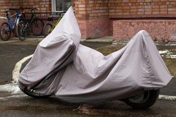 Naklejka premium A motorcycle in a case is standing near the house.Protective cover for motorcycle.