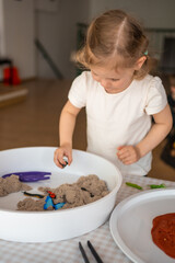 Little girl playing with kinetic sand and toys insect. Sensory development and experiences, themed activities with children, fine motor skills development