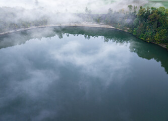 Aerial view of fog above lake early in the morning during sunrise. Misty scenery with reflections.