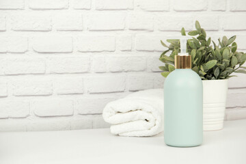 A green plastic bottle of cleaning agent with space for text and white moss twisted towel on a white bricks background.