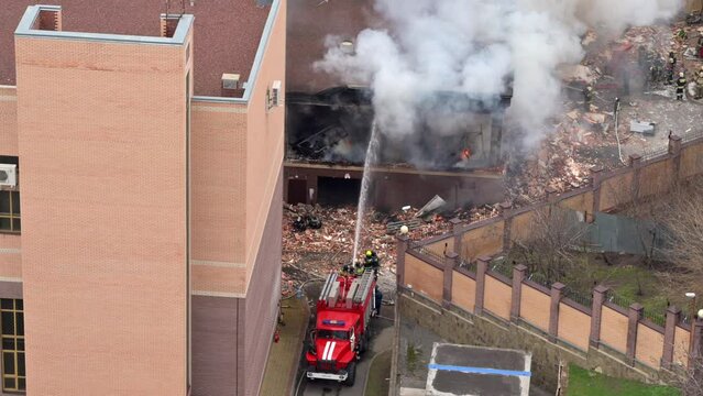 Aerial view of firefighters extinguishing fire in industrial or living area, near high office building after explosion of natural gas