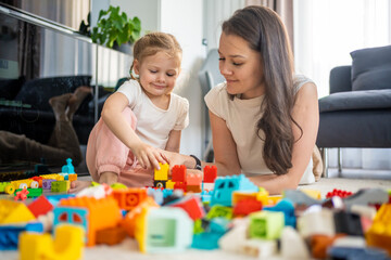 Little girl play with constructor toy on floor in home with mom or woman babysitter, educational game, family at home spend leisure activities time together concept