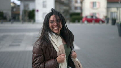 One happy carefree young woman running outside in urban street turning head toward camera in slow motion and smiling