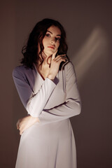 A young brunette woman in a tight dress stands in the studio on a purple background. 