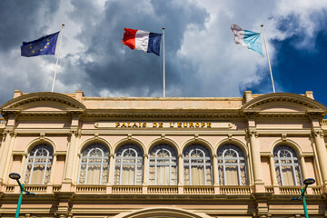 Façade du Palais de l'Europe à Menton éclairé par le soleil malgré de gros nuages sombres