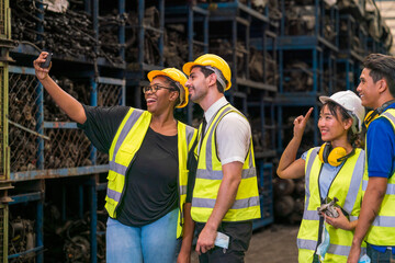 Factory worker and engineer as team. Group of industrial staff taking a selfie on a phone while working in a warehouse factory.