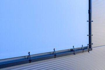 Fragment of the outdoor light blue advertising banner fastened to the black metal frame, mockup