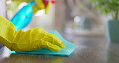 Housewife in yellow rubber gloves wiping wooden table surface in kitchen at home