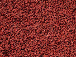 Fototapeta premium Textured background of a red sports surface on a running field. Rubber red granular coating on the sports field. Close-up background of a grainy rubber sports floor.