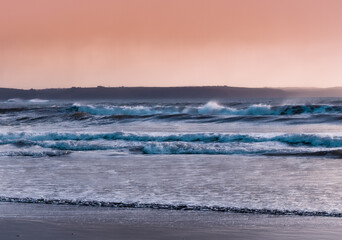 Waves crashing on sandy beach at sunset