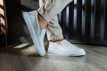Close-up of male feet in white casual shoes. Fashionable young man standing in leather stylish...