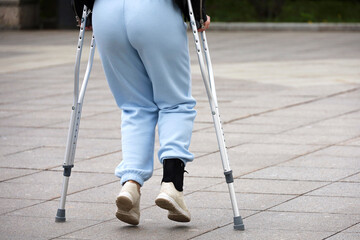 Woman walking with crutches on a city street, female legs on sidewalk. Leg injury, fracture or...
