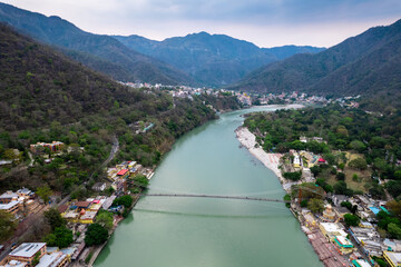 aerial drone shot of blue water of river ganga stretching into distance with himalayas with ram setu suspension bridge and temples on the banks of the river © Memories Over Mocha