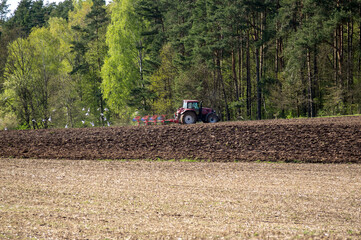 Rolnictwo traktor na polu w czasie orki ptactwo latające nad zaoraną ziemia uprawną.