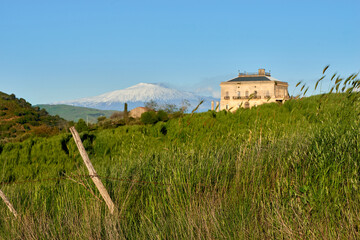 a manor house on the green meadows in the valleys of Sicily with the snow-capped Etna volcano as a background in spring