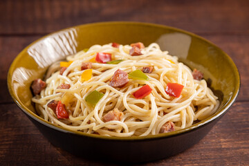 Plate with spaghetti, bacon and chopped vegetables.